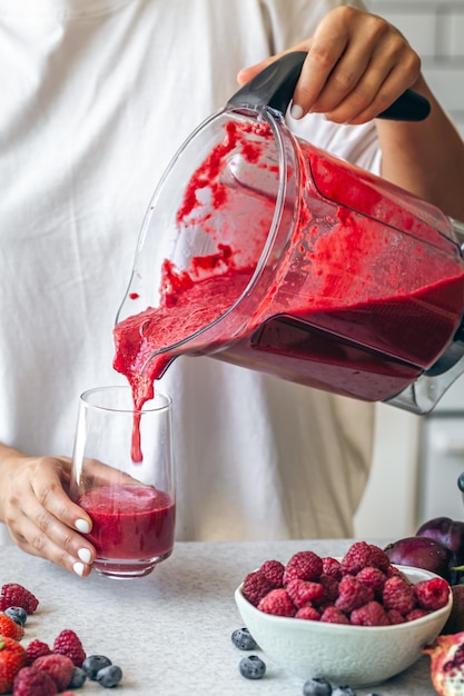 Uma mulher despeja um smoothie de bagas de um liquidificador em um copo