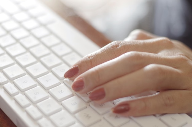 Uma mulher digitando em um teclado com manicure vermelha nas unhas.