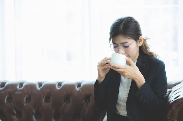 Uma mulher do sudeste asiático vestindo um terno e bebendo bebidas quentes no sofá