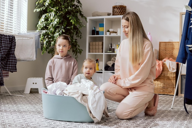 Uma mulher e duas filhas com cabelo loiro e bronze dobram a roupa limpa da secadora