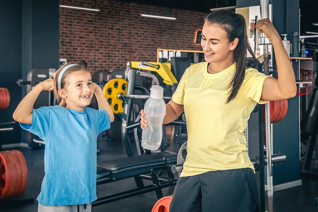 Uma mulher e filha estão mostrando seus bíceps malhando na academia