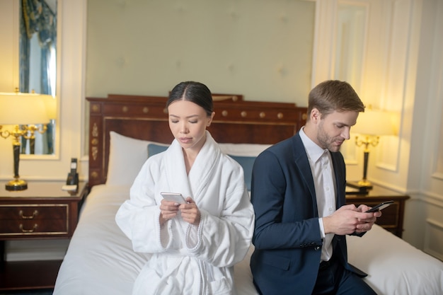 Uma mulher e um homem usando seus smartphones no quarto