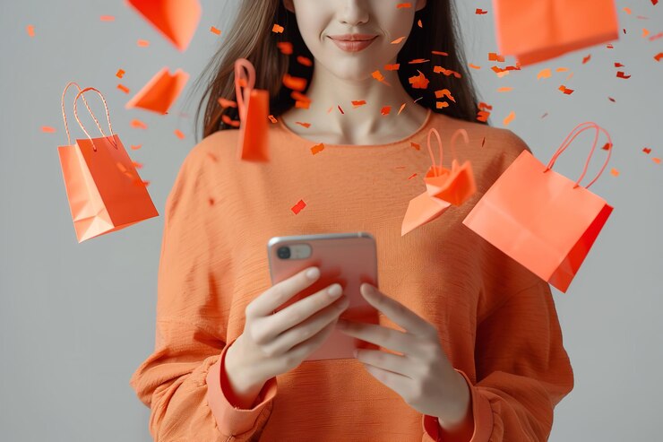 Foto uma mulher é vista em close-up agarrando um telefone celular e pequenos sacos de compras laranjas são vistos emergindo dele contra um fundo branco simples.