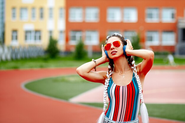 Uma mulher elegante de óculos escuros e fones de ouvido grandes ouve música no estádio.