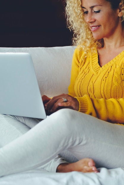 Uma mulher em casa sentada no sofá navegando na web e usando laptop em atividade de conexão de tecnologia de lazer Mulheres modernas escrevendo no computador sozinhas confortavelmente no sofá e sorrindo