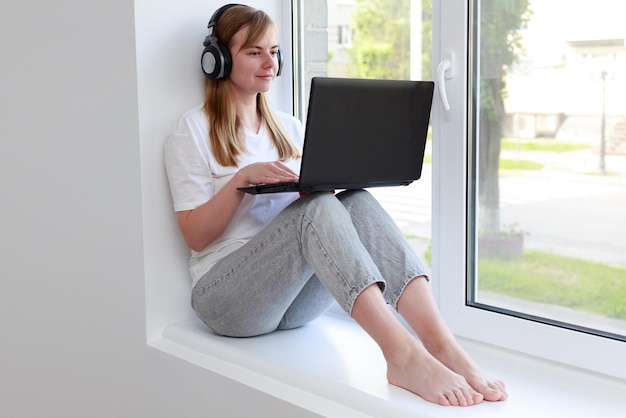 Uma mulher em fones de ouvido com um laptop trabalhando na janela