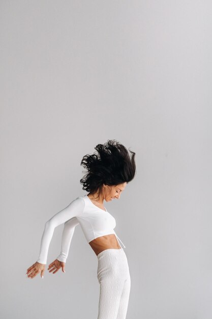 Uma mulher em roupas esportivas brancas está envolvida em meditação kali dinâmica no salão de ioga
