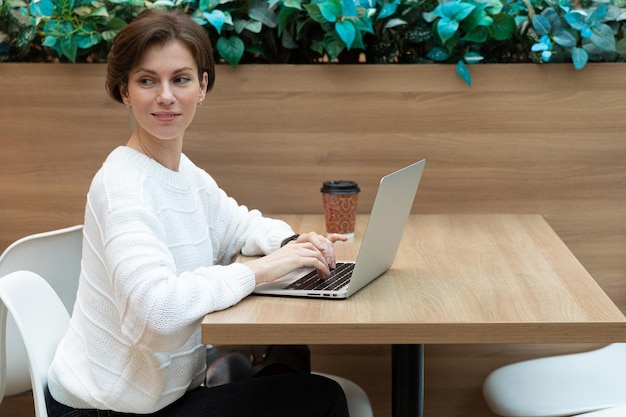 Uma mulher em um café está esperando um parceiro de negócios sentado em um laptop