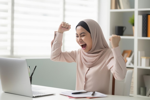 Uma mulher em um hijab comemorando a vitória e o sucesso muito animada com os braços erguidos Generative AI