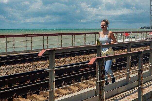 uma mulher em um terno azul de treinamento e com uma garrafa de água corre na ferrovia na estação quente