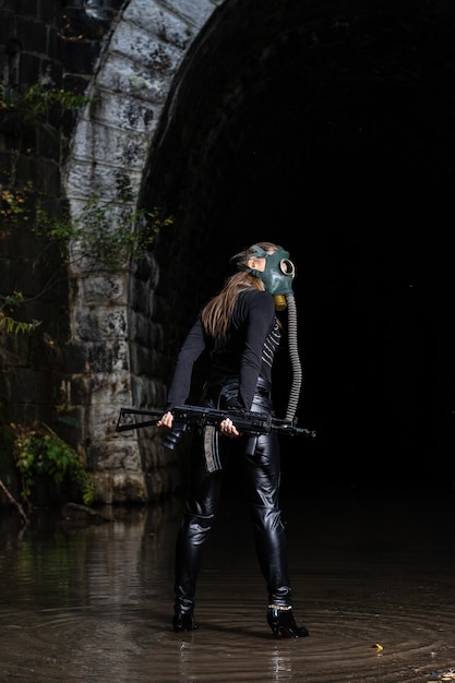 Uma mulher em um terno preto e máscara de gás com uma metralhadora nas mãos
