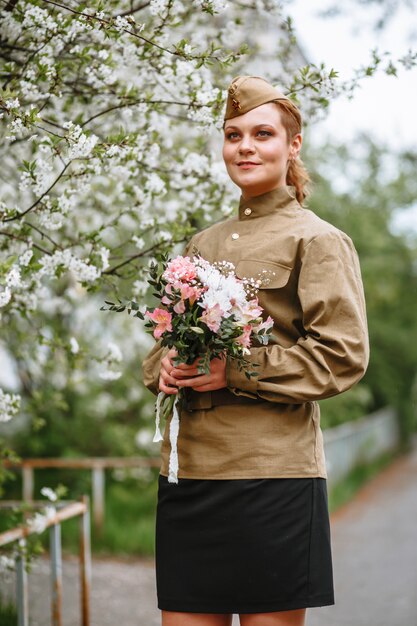 Uma mulher em um uniforme militar soviético ao lado de uma árvore