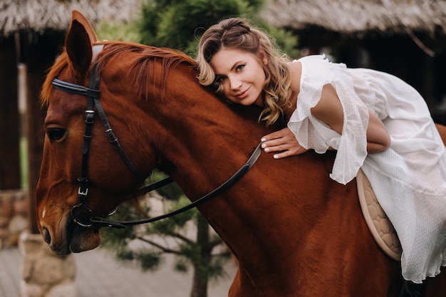 Uma mulher em um vestido branco andando a cavalo perto de uma fazenda