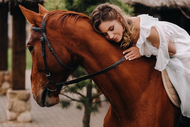 Uma mulher em um vestido branco andando a cavalo perto de uma fazenda