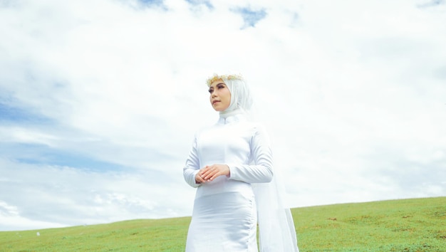 Foto uma mulher em um vestido branco está em um campo com o céu atrás dela.