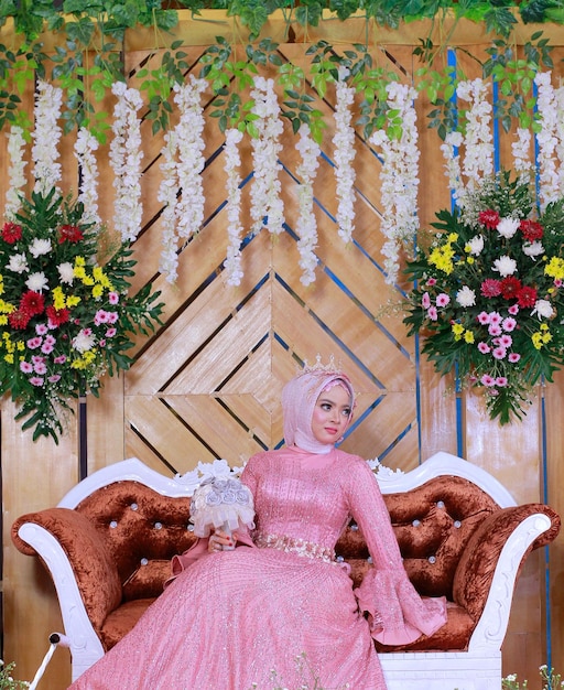Uma mulher em um vestido de casamento muçulmano rosa segurando flores