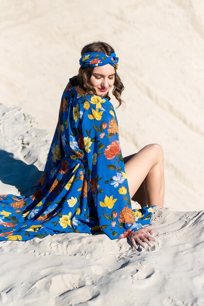 Uma mulher em um vestido floral azul senta-se em uma duna de areia.