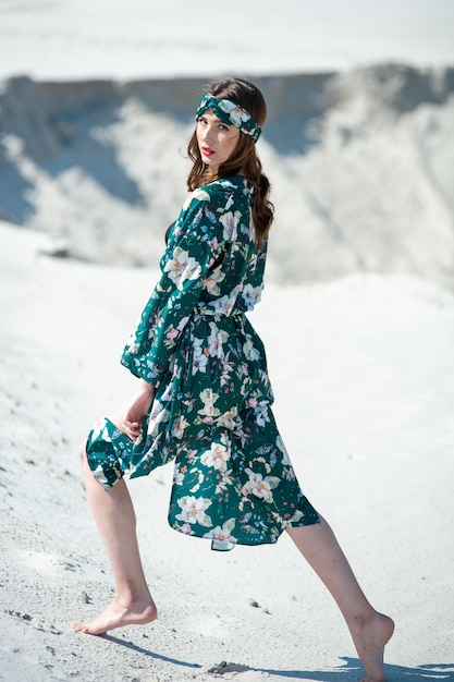 Uma mulher em um vestido floral verde está na areia.