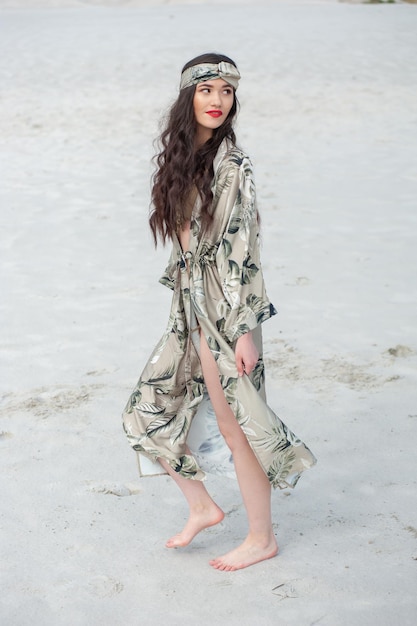 Uma mulher em um vestido longo fica na praia em frente ao oceano.