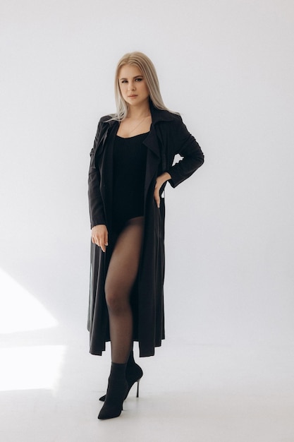 Uma mulher em um vestido preto e meia-calça preta está na frente de um fundo branco.