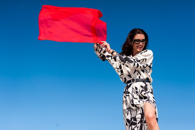 Uma mulher em um vestido segura uma bandeira vermelha na frente de um céu azul.