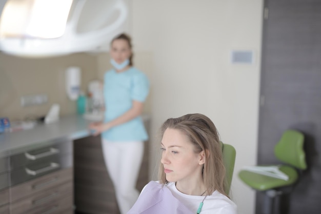 Uma mulher em uma cadeira odontológica com um dentista ao fundo