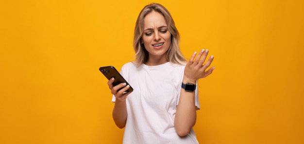 Uma mulher em uma camiseta branca com um smartphone nas mãos usa um aplicativo em um fundo amarelo