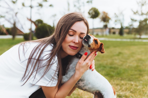 Uma mulher em uma camiseta branca e jeans abraça seu cachorro Jack Russell Terrier na natureza no parque Leais melhores amigos desde a infância Estilo de vida