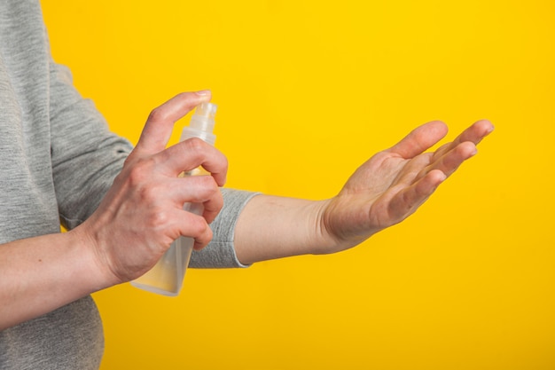 Uma mulher em uma máscara médica desinfeta as mãos com um desinfetante em um fundo amarelo, estúdio
