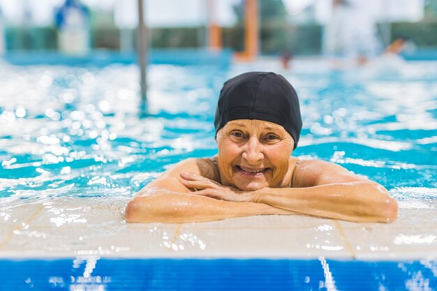 Uma mulher em uma piscina com um boné na cabeça e um sorriso no rosto.