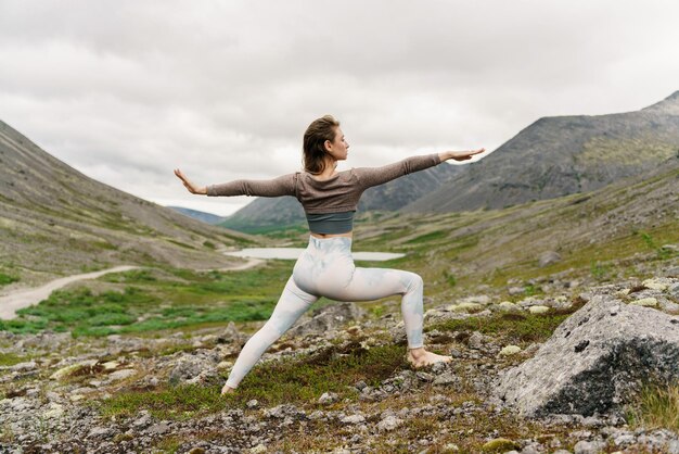 Uma mulher esbelta é uma treinadora realizando o exercício yoga asana nas montanhas