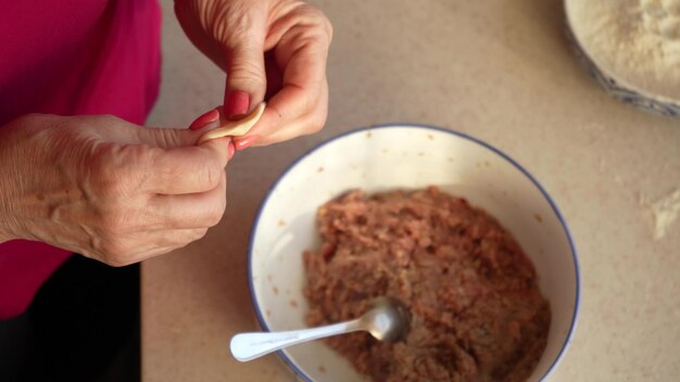 Uma mulher esculpe bolinhos com as próprias mãos de massa e carne picada em uma cozinha caseira cozinhando comida caseira