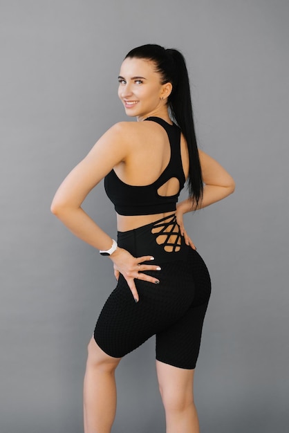 Foto uma mulher esportiva com uma figura perfeita e nádegas em um terno preto segura as mãos abaixo da cintura