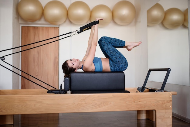 Uma mulher esportiva em roupas esportivas está fazendo Pilates em um reformador no ginásioVista lateral