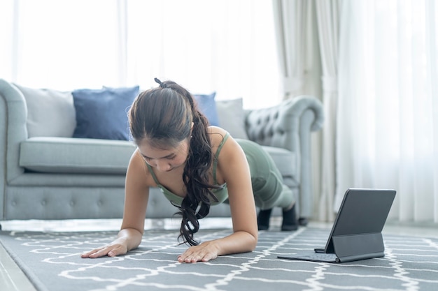 Uma mulher esportiva em roupas esportivas se exercita enquanto assiste a uma sessão de exercícios on-line em seu tablet em casa