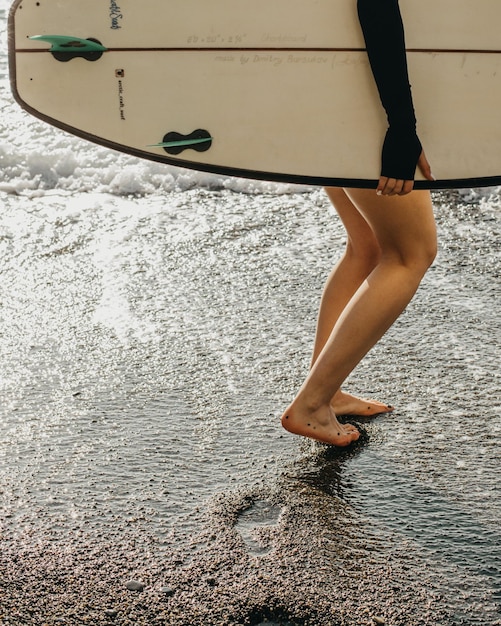 Foto uma mulher está caminhando na praia com uma prancha de surf.