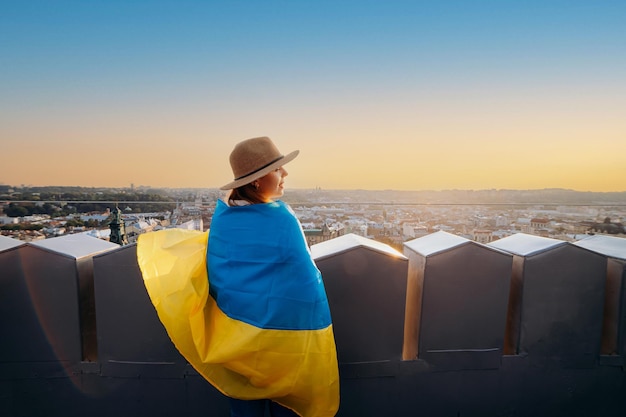 Uma mulher está com a bandeira nacional ucraniana e acenando rezando pela paz ao pôr do sol em LvivxAA símbolo da independência e força do povo ucraniano Ore pela Ucrânia