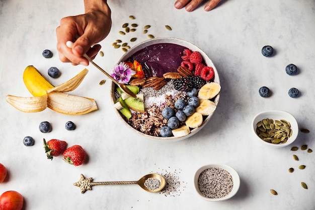 Uma mulher está comendo uma tigela de açaí com frutas frescas no café da manhã com mirtilos de banana amoras