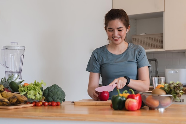 Uma mulher está cortando uma maçã em uma tábua de corte de madeira em uma cozinha ela está sorrindo e ela está