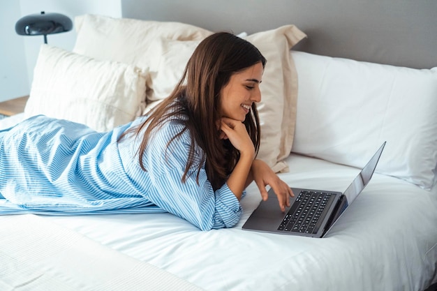 uma mulher está deitada em uma cama com um laptop