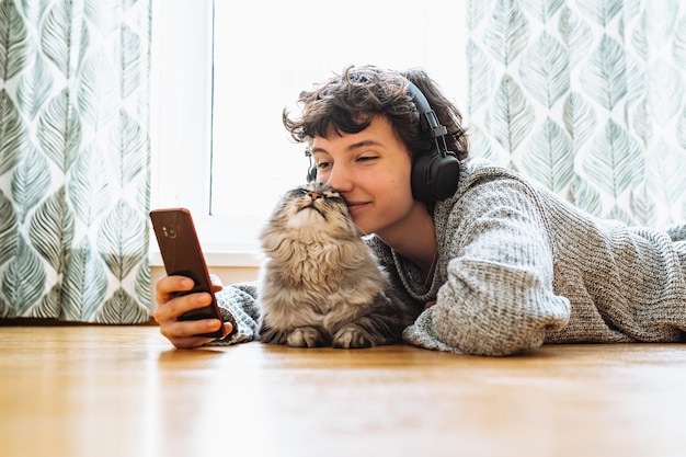 Uma mulher está deitada no chão com seu gato e usando fones de ouvido.