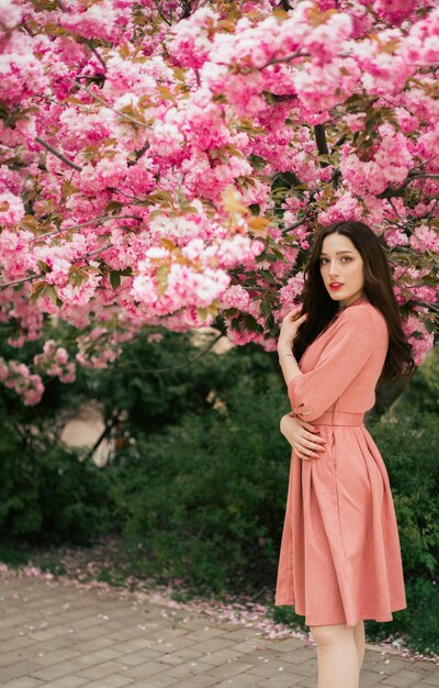 Uma mulher está em frente a uma árvore florida em um vestido rosa.