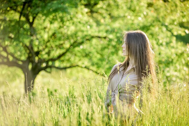 uma mulher está em um campo de grama alta com árvores no fundo