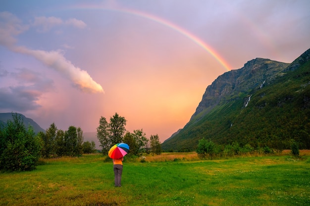 Uma mulher está em um gramado entre as montanhas sob um guarda-chuva após a chuva