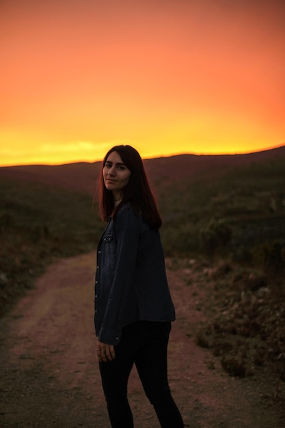 Uma mulher está em uma estrada de terra em frente a um pôr do sol