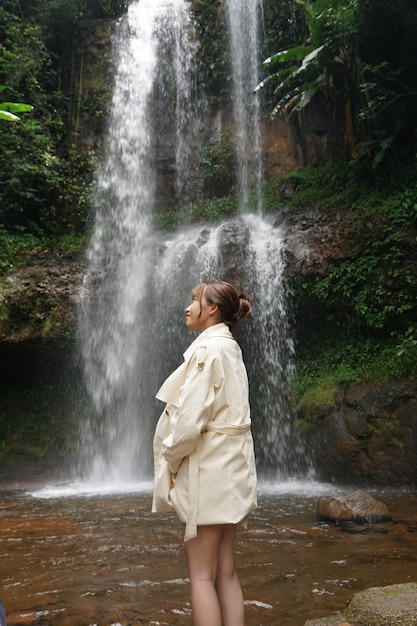 Uma mulher está em uma poça de água em frente a uma cachoeira.