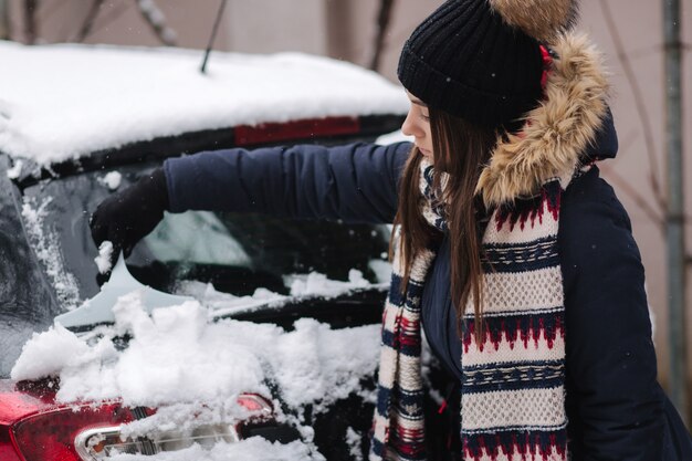 Uma mulher está limpando a janela de neve de um carro com um raspador de neve.