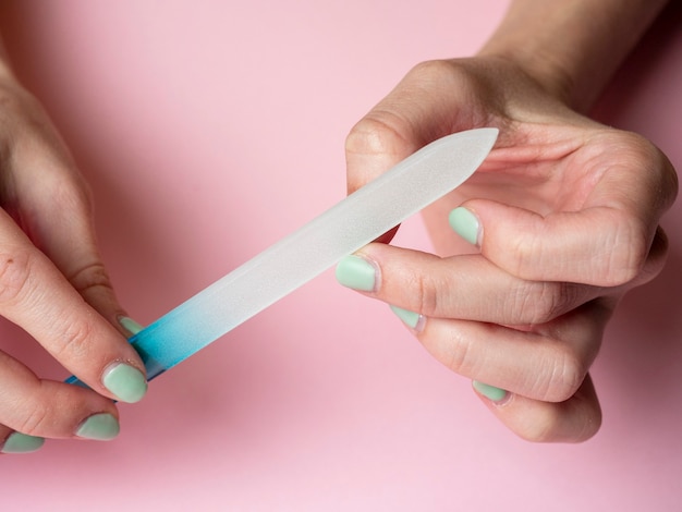 Uma mulher está lixando as unhas com uma lixa de unha em um fundo rosa. Cuidados com as unhas em casa. Beleza e Saúde