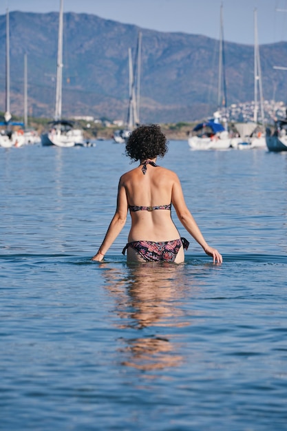 Uma mulher está nadando na água na frente de um veleiros.