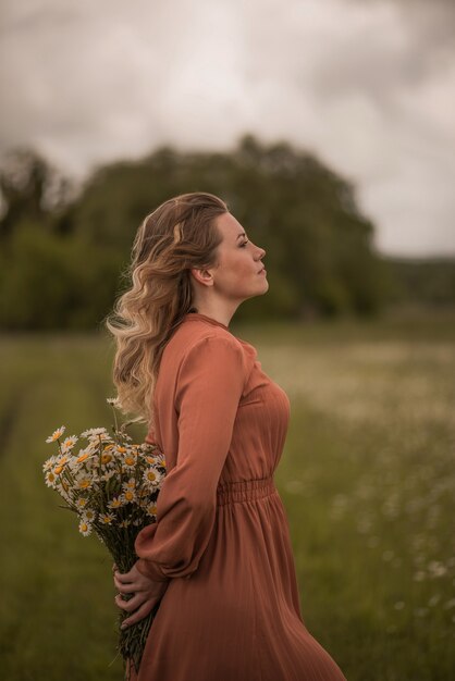 Uma mulher está no meio de um campo com um buquê de margaridas nas mãos.